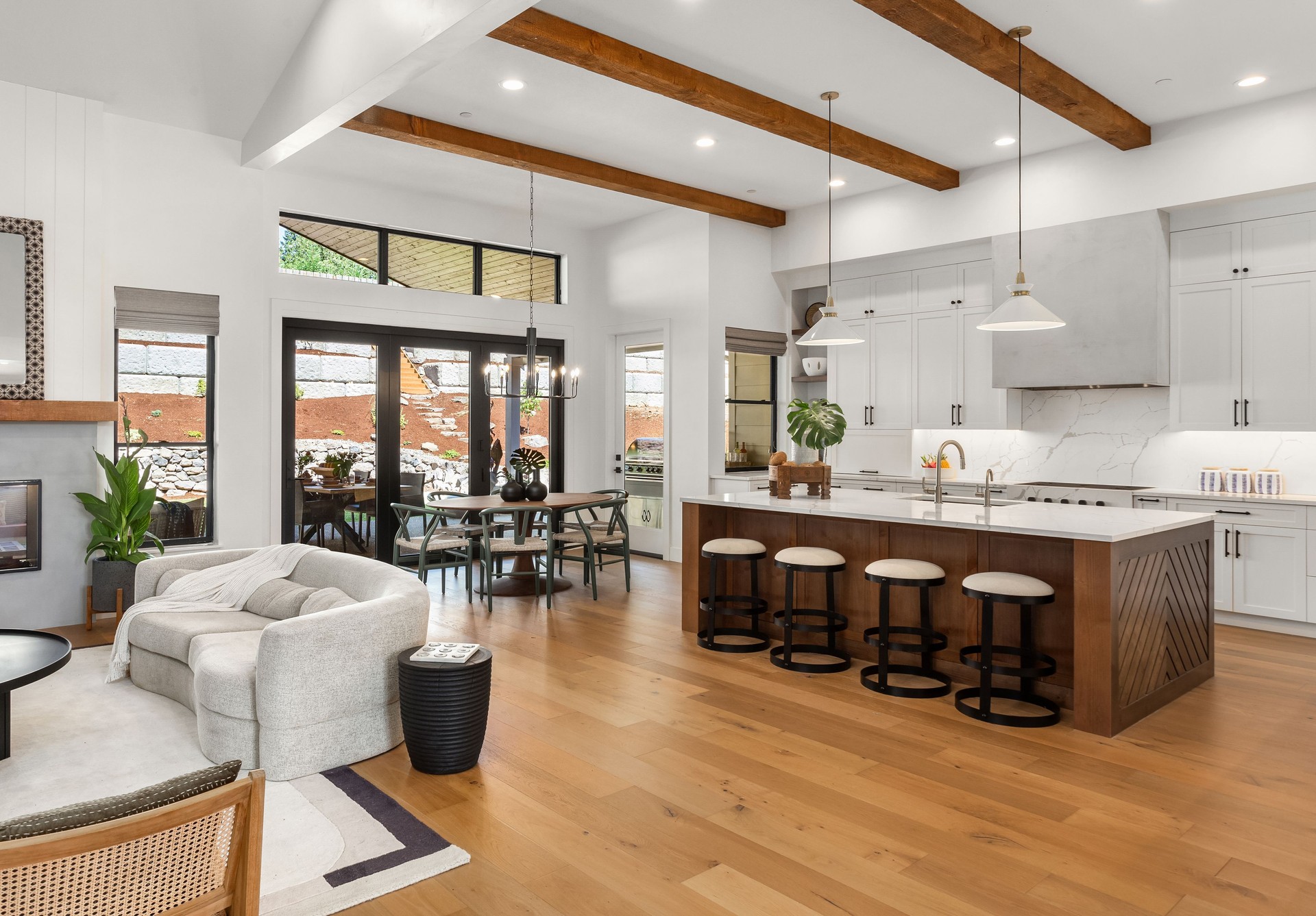 Beautiful living room and kitchen in new luxury home with white cabinets, wood beams, pendant lights and hardwood floors